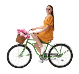 Photo of Smiling woman in sunglasses riding bicycle with basket of peony flowers on white background