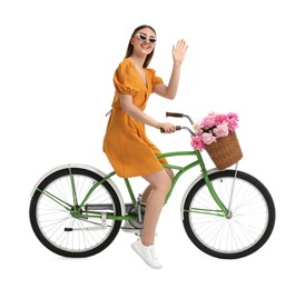 Photo of Smiling woman in sunglasses riding bicycle with basket of peony flowers on white background