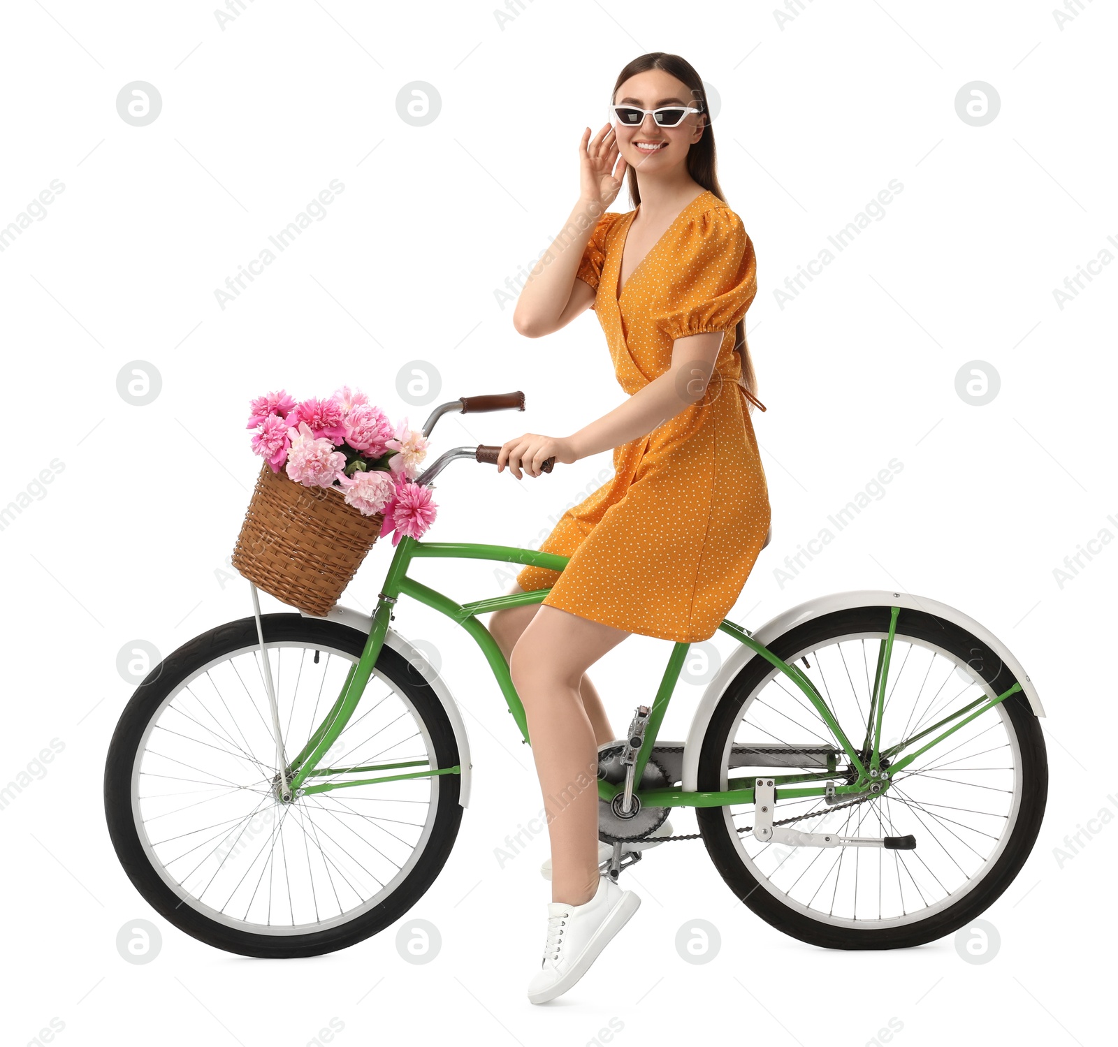 Photo of Smiling woman in sunglasses riding bicycle with basket of peony flowers on white background