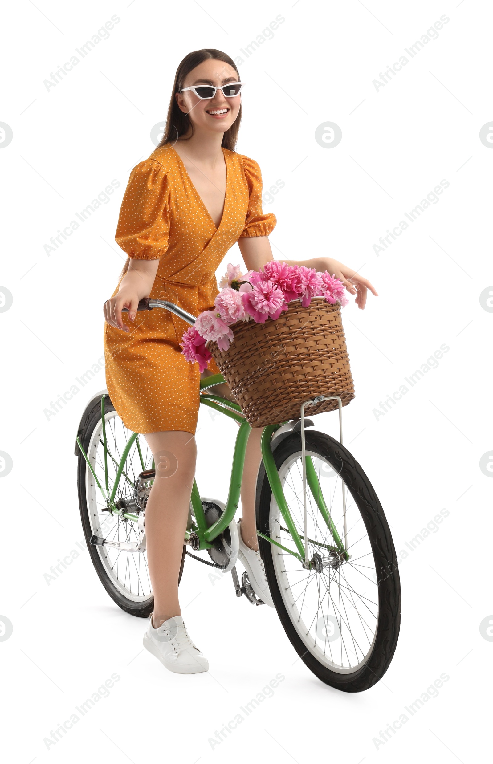 Photo of Smiling woman in sunglasses riding bicycle with basket of peony flowers on white background