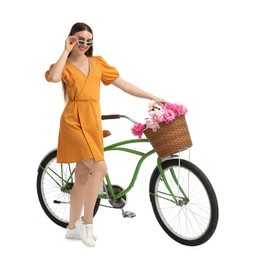 Photo of Smiling woman in sunglasses with bicycle and basket of peony flowers isolated on white