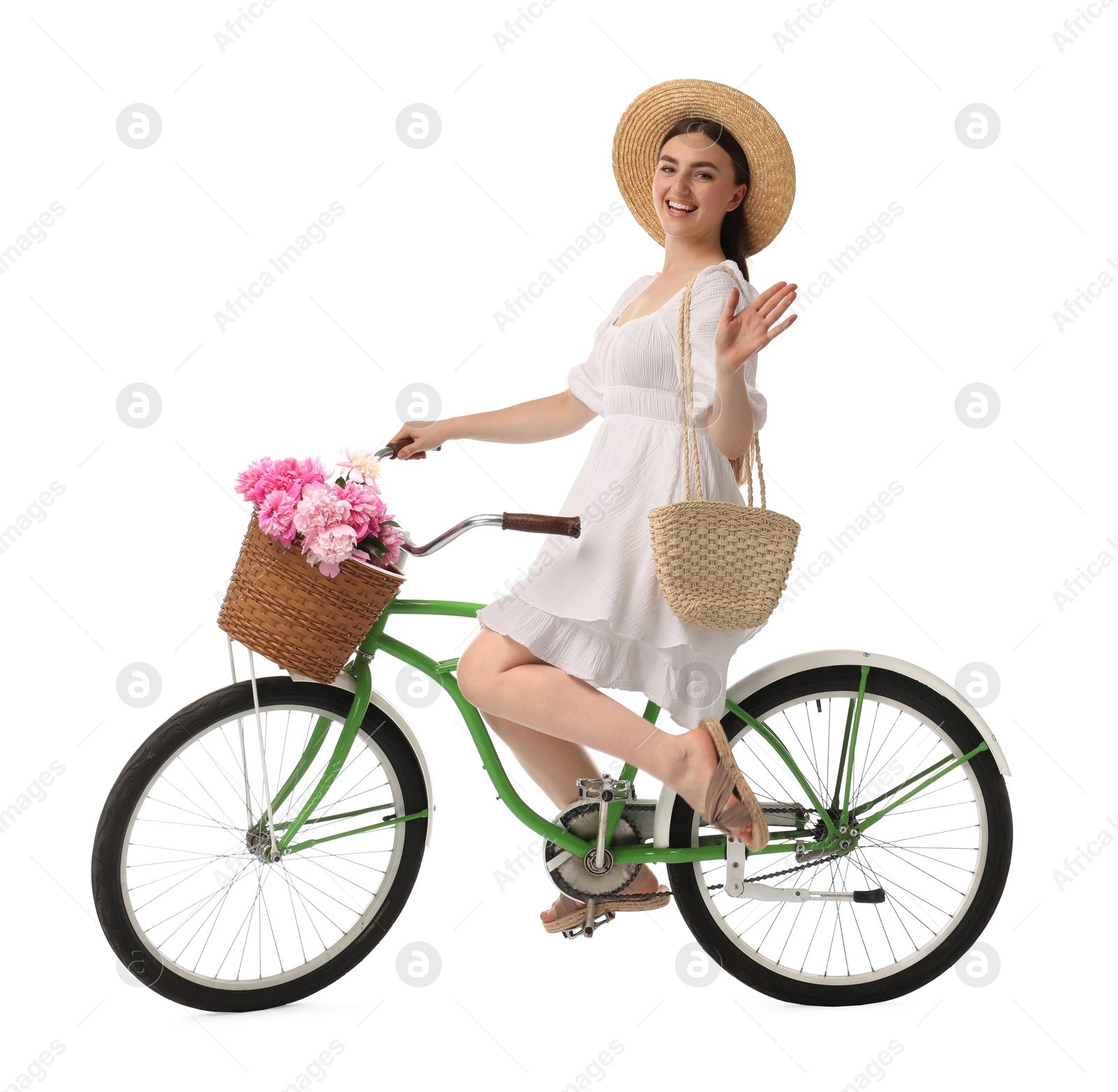 Photo of Smiling woman riding bicycle with basket of peony flowers on white background