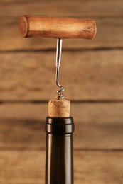 Photo of Wine bottle with corkscrew on wooden background, closeup