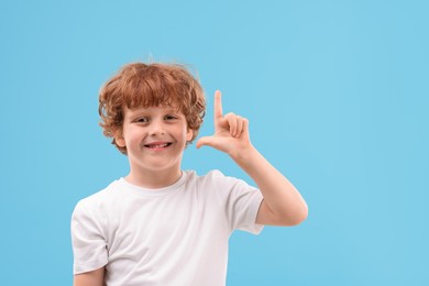 Photo of Portrait of cute little boy pointing at something on light blue background