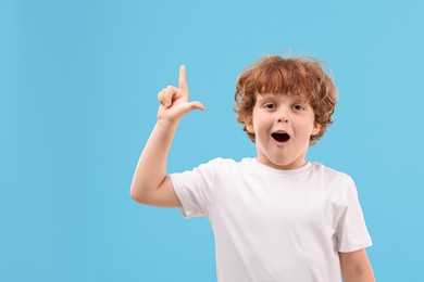 Photo of Portrait of emotional little boy pointing at something on light blue background