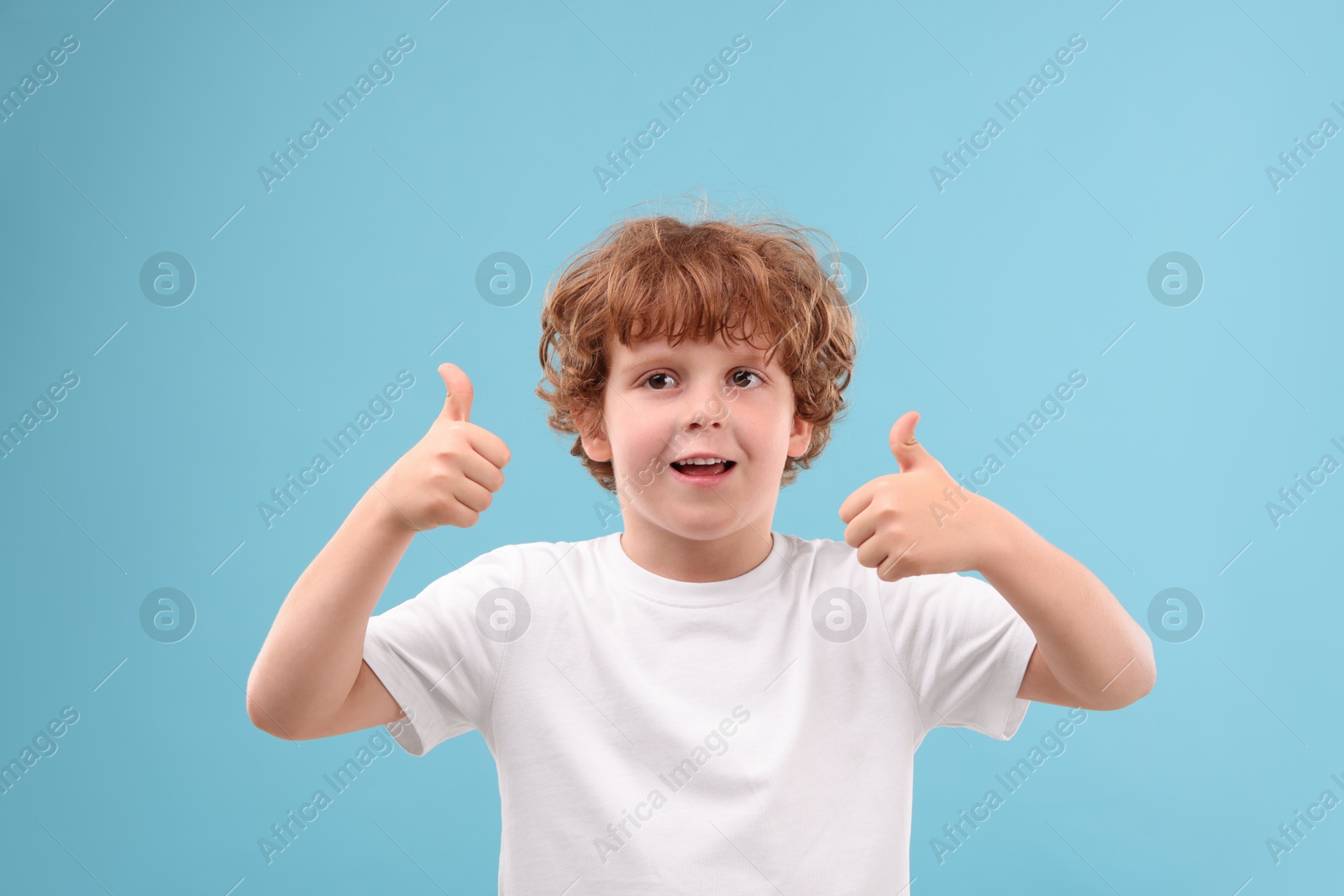 Photo of Portrait of cute little boy showing thumbs up on light blue background