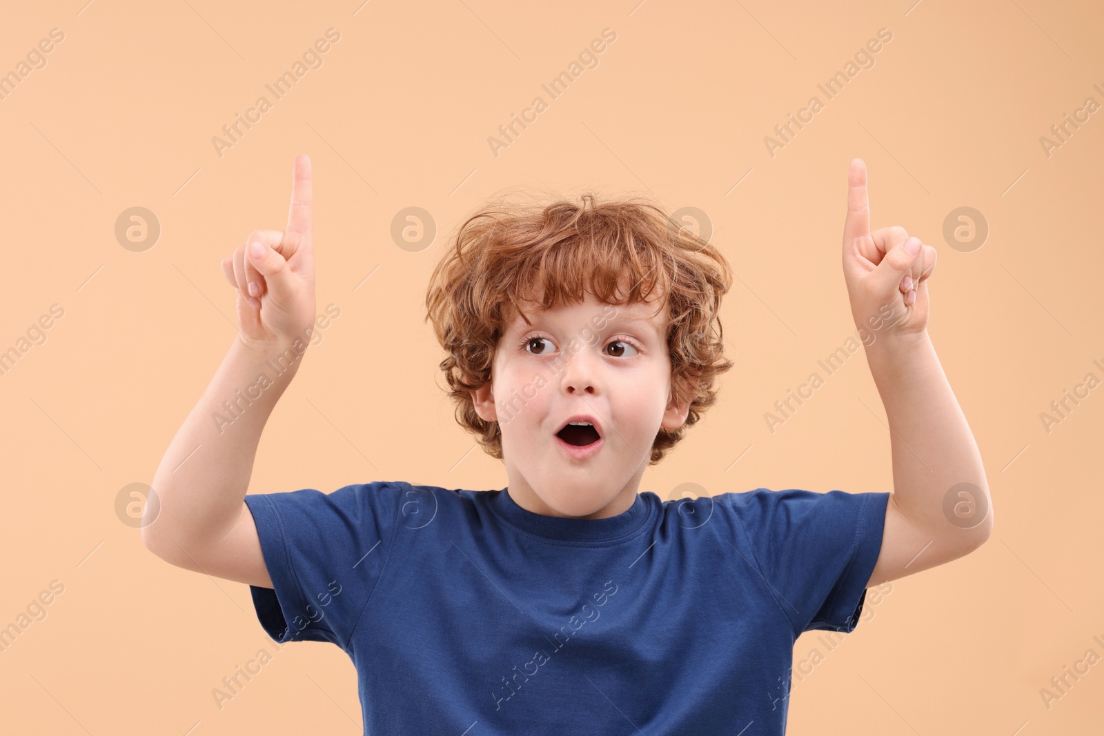 Photo of Portrait of emotional little boy pointing at something on beige background