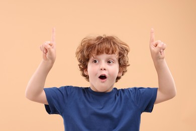 Photo of Portrait of emotional little boy pointing at something on beige background