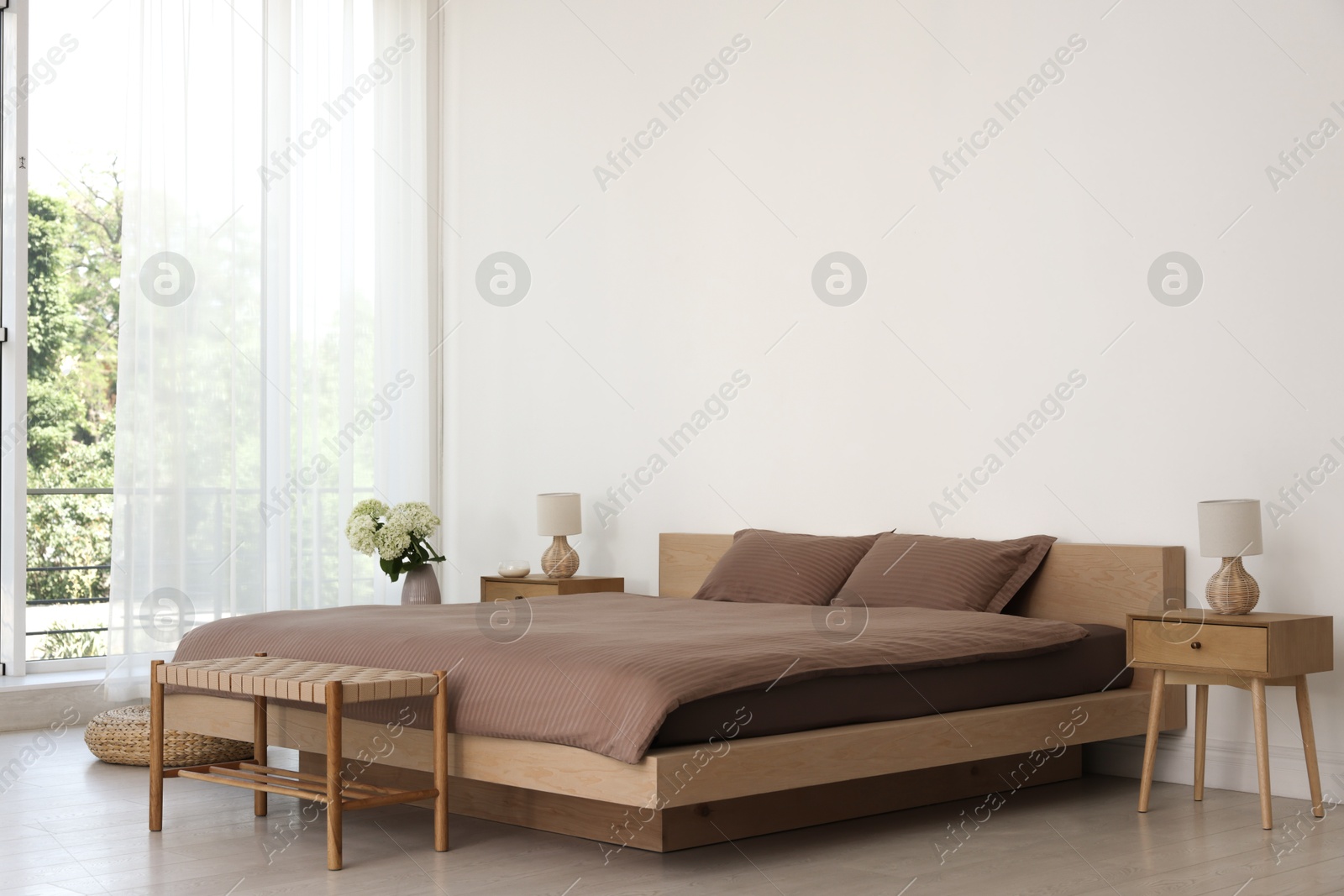 Photo of Stylish bedroom interior with large bed, ottoman and bedside tables