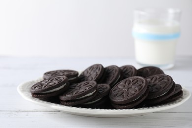 Tasty sandwich cookies and milk on white wooden table