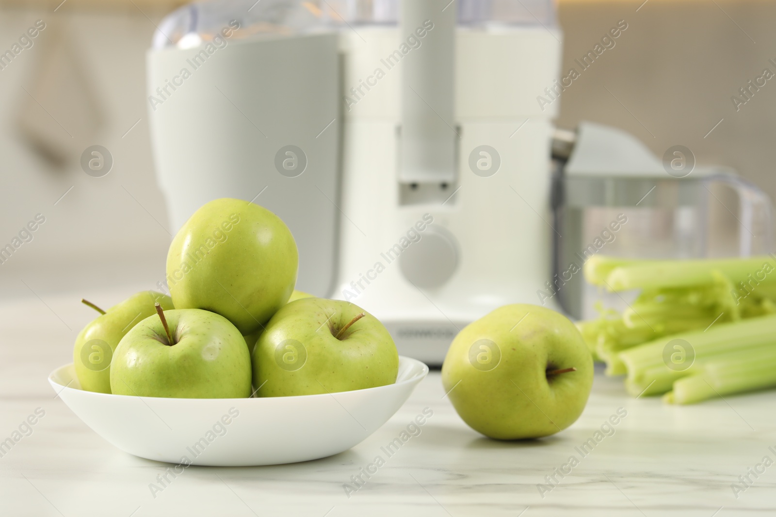 Photo of Modern juicer, celery and apples on white marble table in kitchen, selective focus