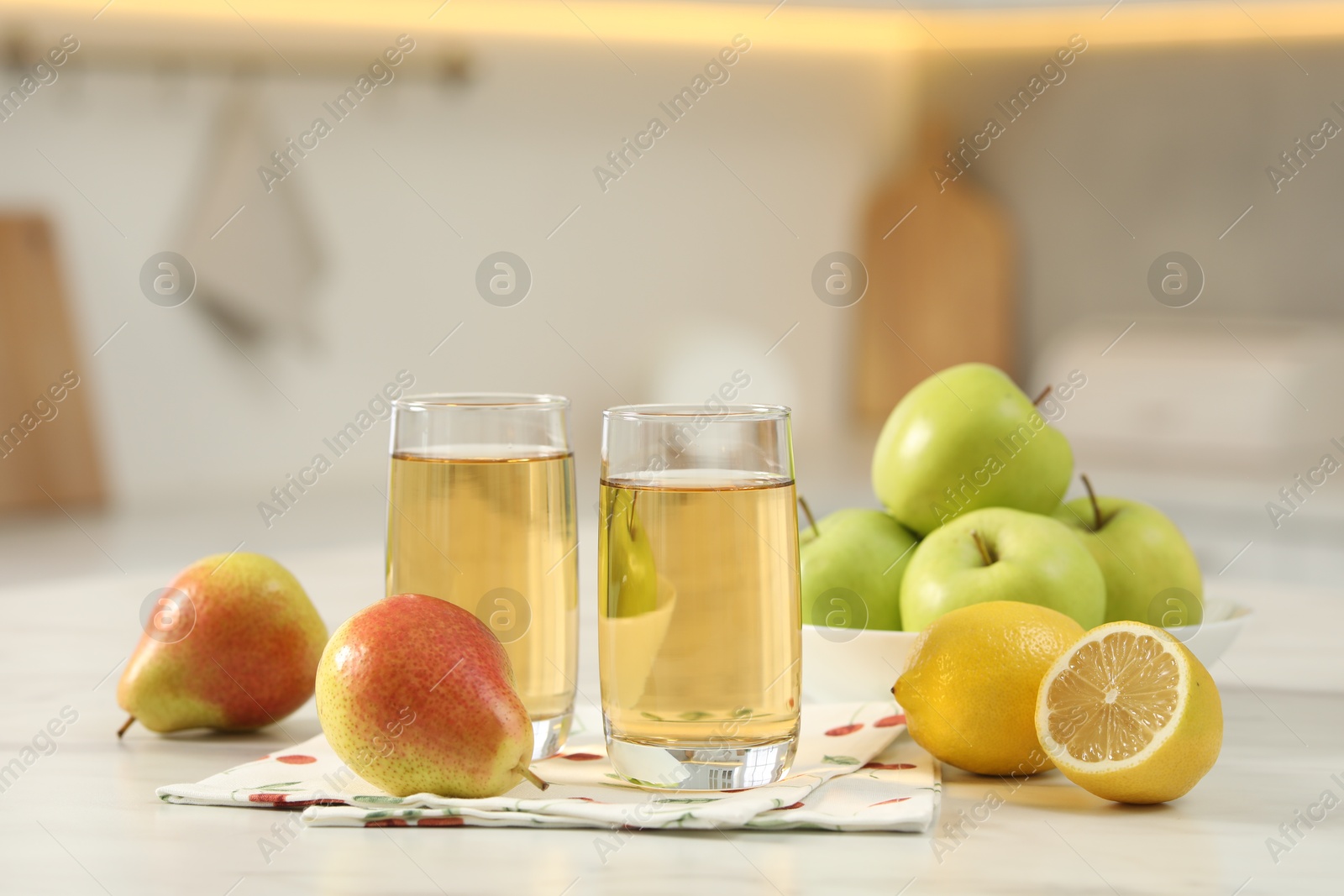 Photo of Glasses of fresh juice and fruits on white marble table in kitchen