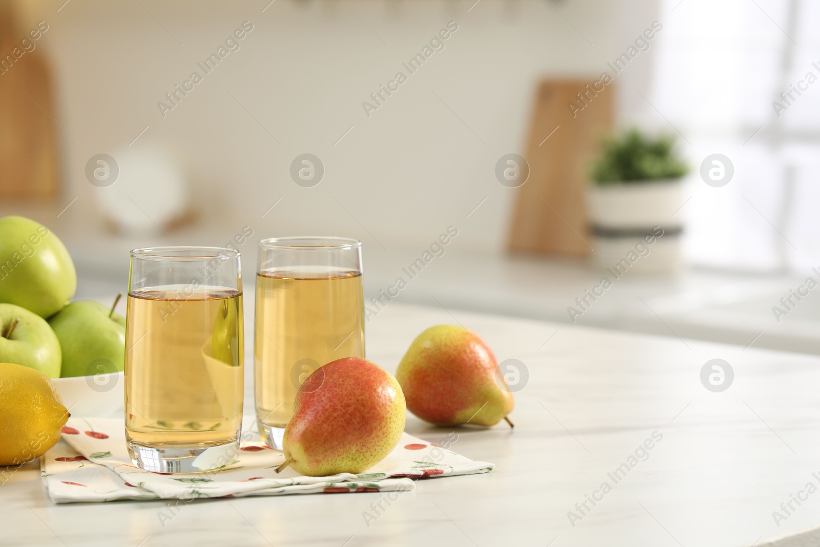 Photo of Glasses of fresh juice and fruits on white marble table in kitchen, space for text