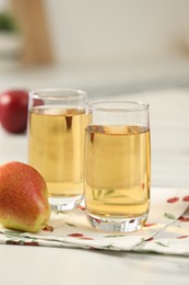 Glasses of fresh juice, pears and apples on white marble table in kitchen