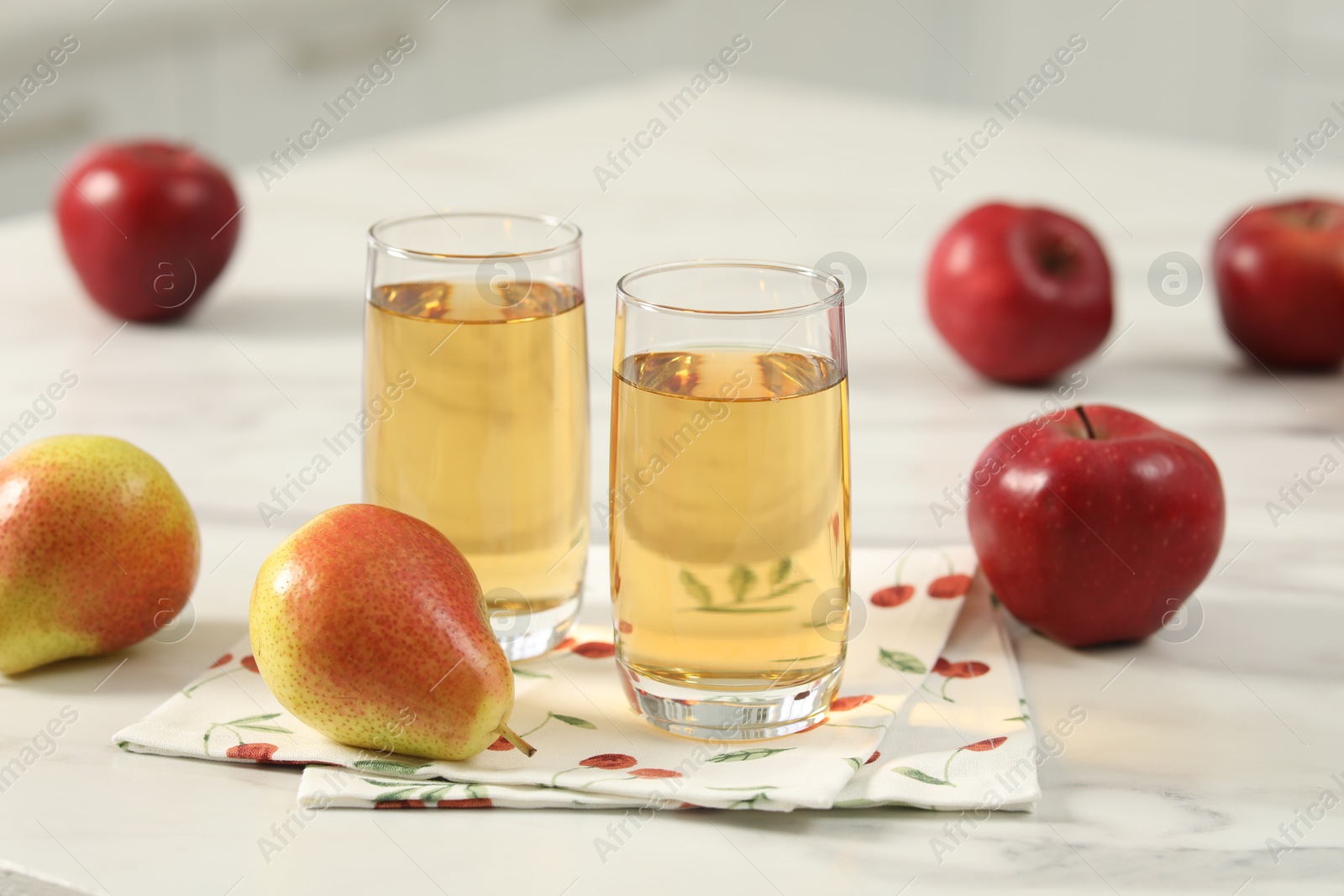 Photo of Glasses of fresh juice, pears and apples on white marble table in kitchen