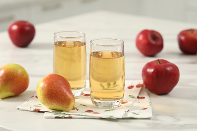 Glasses of fresh juice, pears and apples on white marble table in kitchen