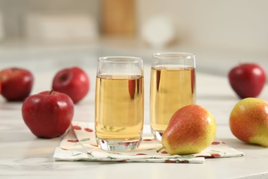 Photo of Glasses of fresh juice, pears and apples on white marble table in kitchen