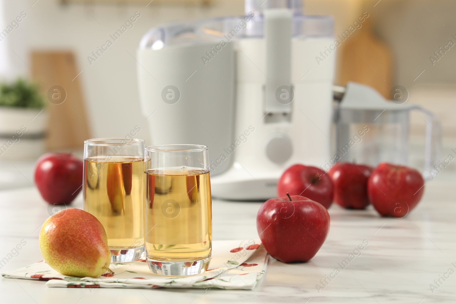 Photo of Glasses of fresh juice, pears, apples and modern juicer on white marble table in kitchen, selective focus