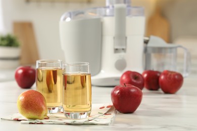 Photo of Glasses of fresh juice, pears, apples and modern juicer on white marble table in kitchen, selective focus