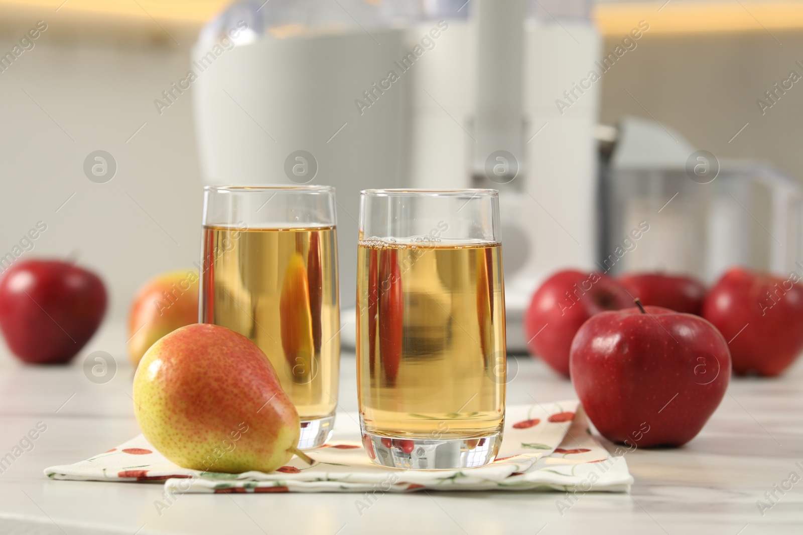 Photo of Glasses of fresh juice, pears, apples and modern juicer on white marble table in kitchen, selective focus