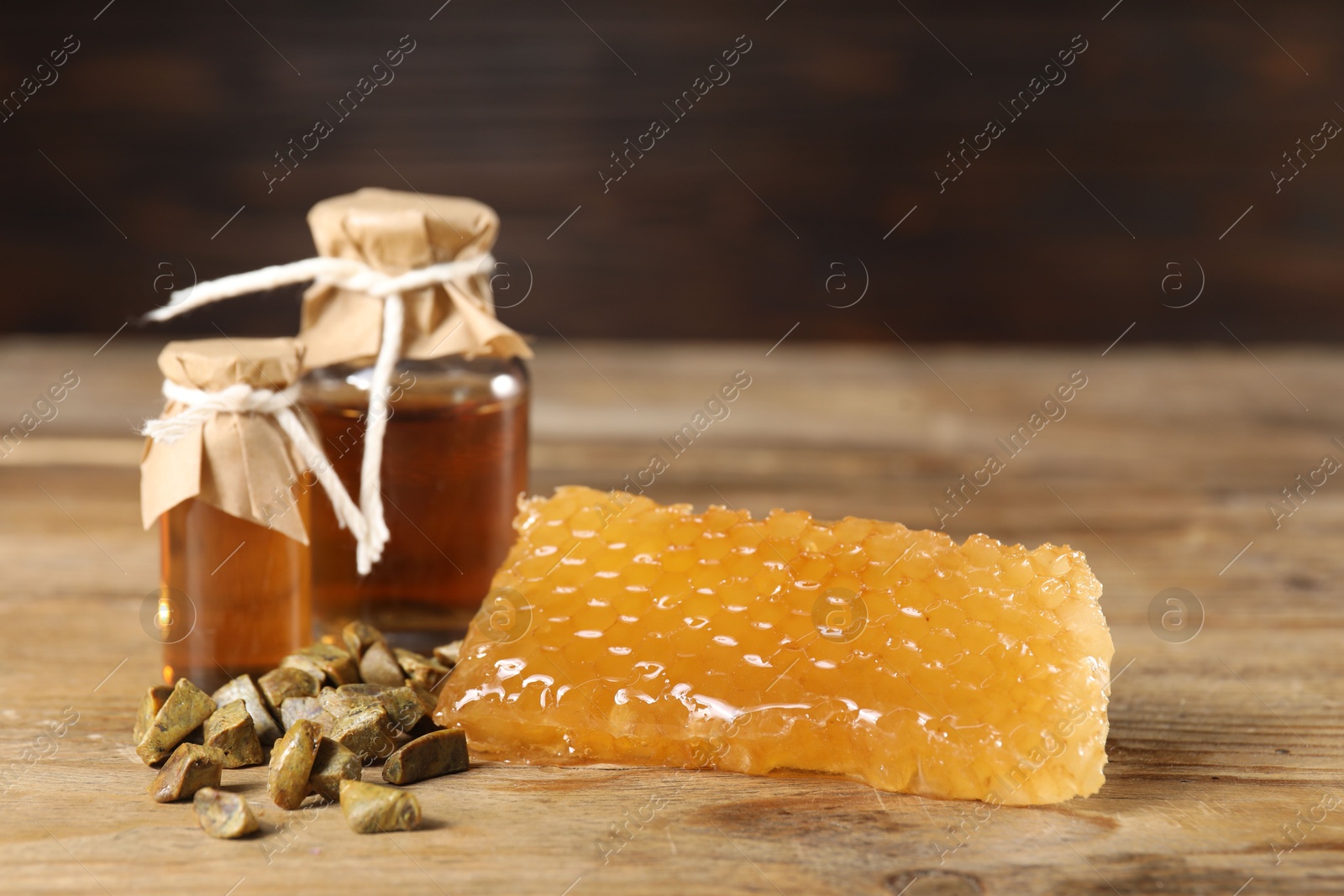 Photo of Natural honey tincture, propolis granules and sweet honeycomb on wooden table, closeup