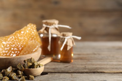 Photo of Natural honey tincture, propolis granules and sweet honeycombs on wooden table, closeup. Space for text