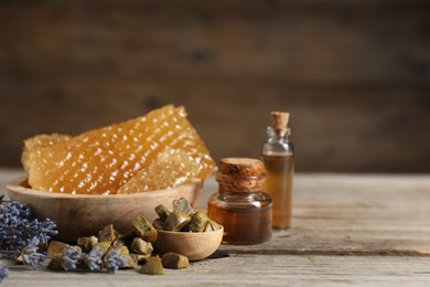 Photo of Natural honey tincture, lavender, propolis granules and sweet honeycombs on wooden table, closeup. Space for text