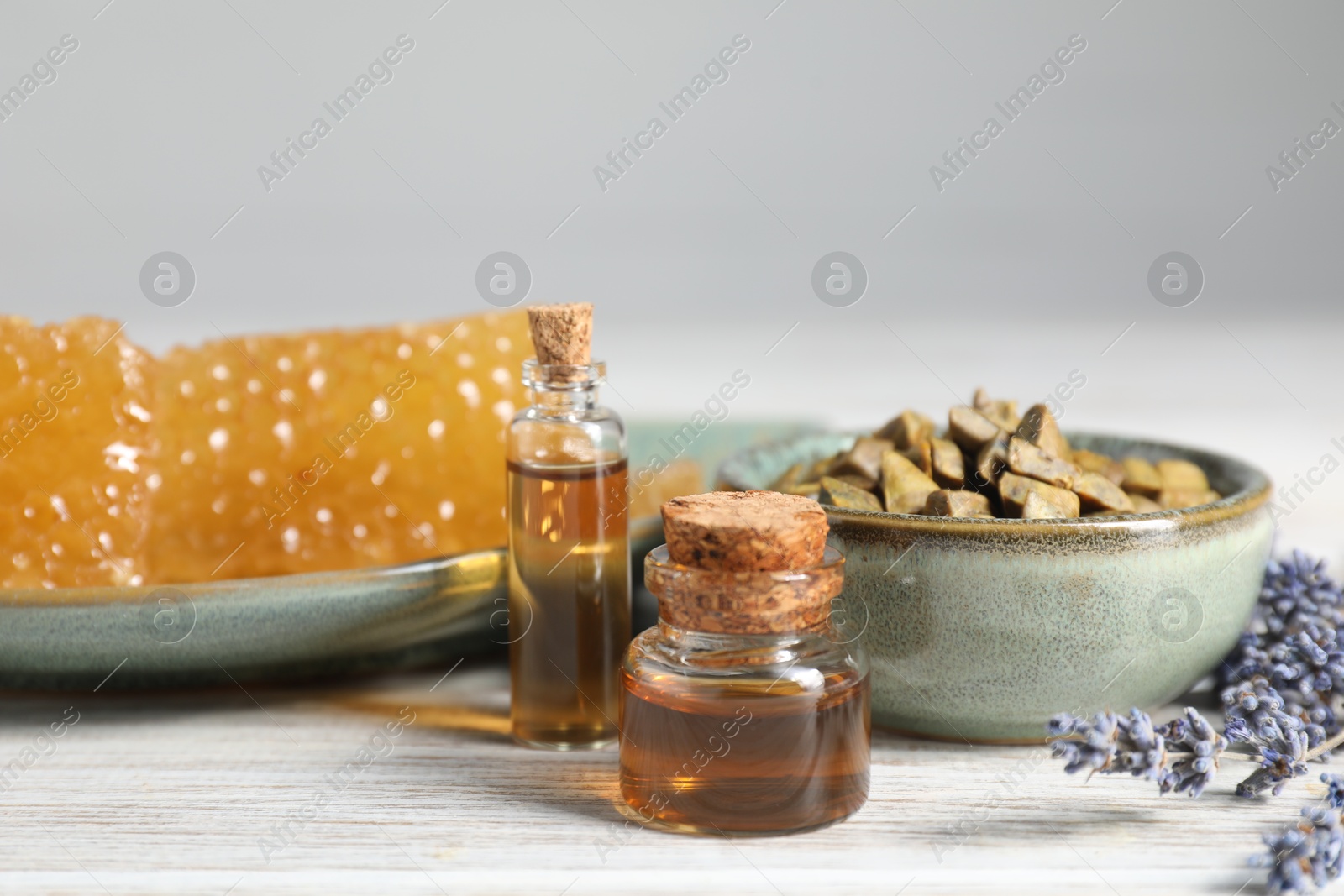 Photo of Natural honey tincture, lavender, propolis granules and sweet honeycombs on white wooden table, closeup