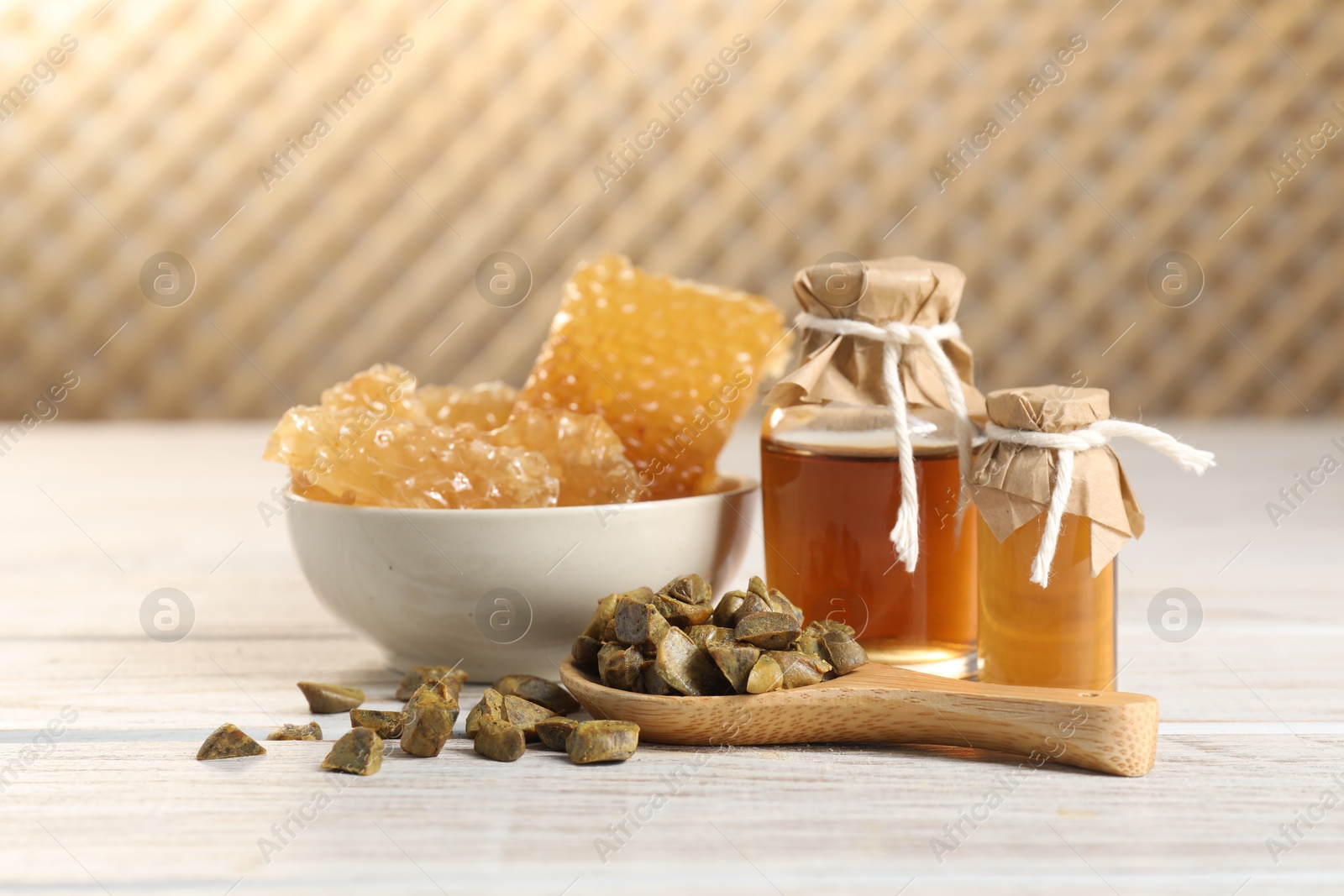 Photo of Natural honey tincture, propolis granules and sweet honeycombs on white wooden table