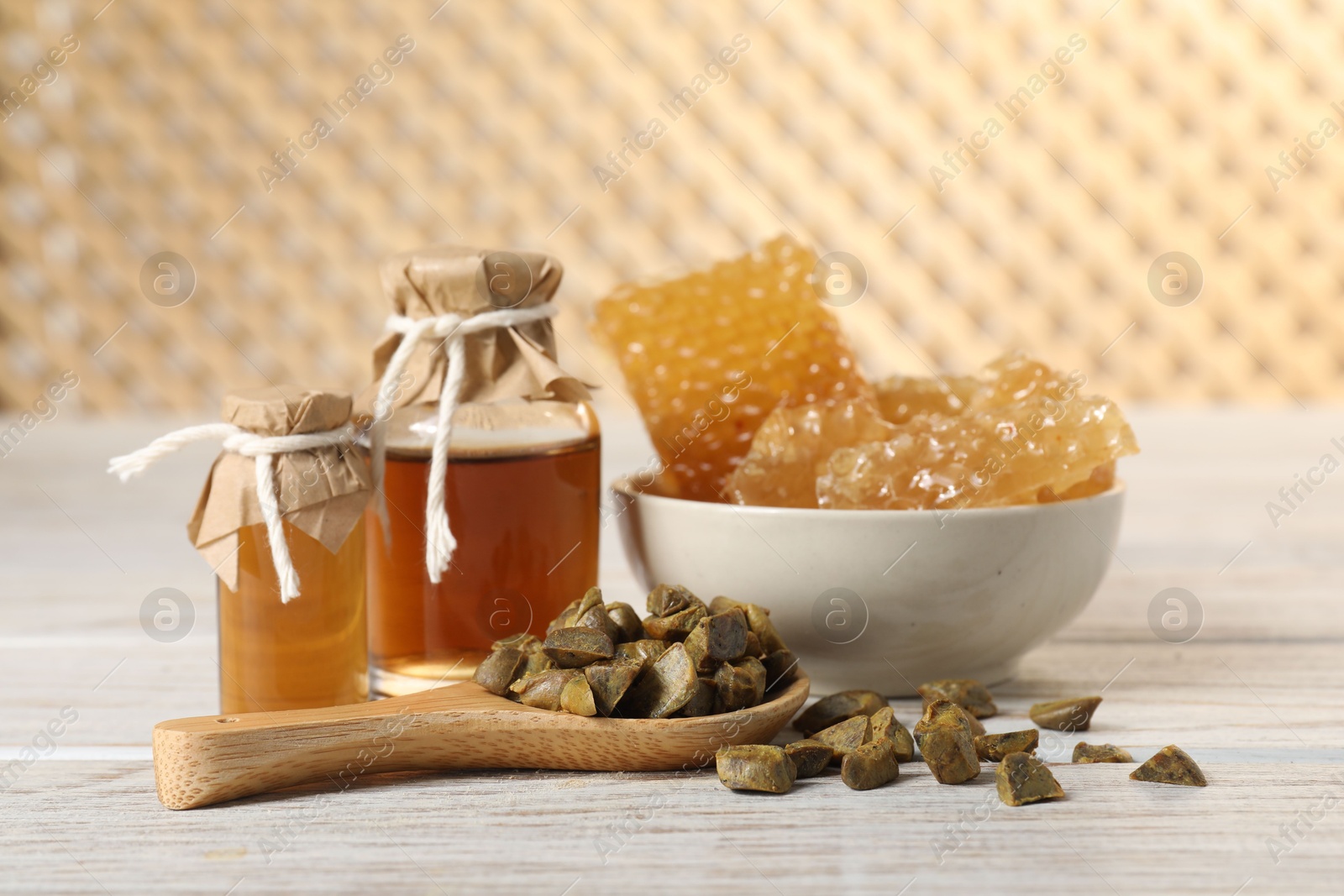 Photo of Natural honey tincture, propolis granules and sweet honeycombs on white wooden table