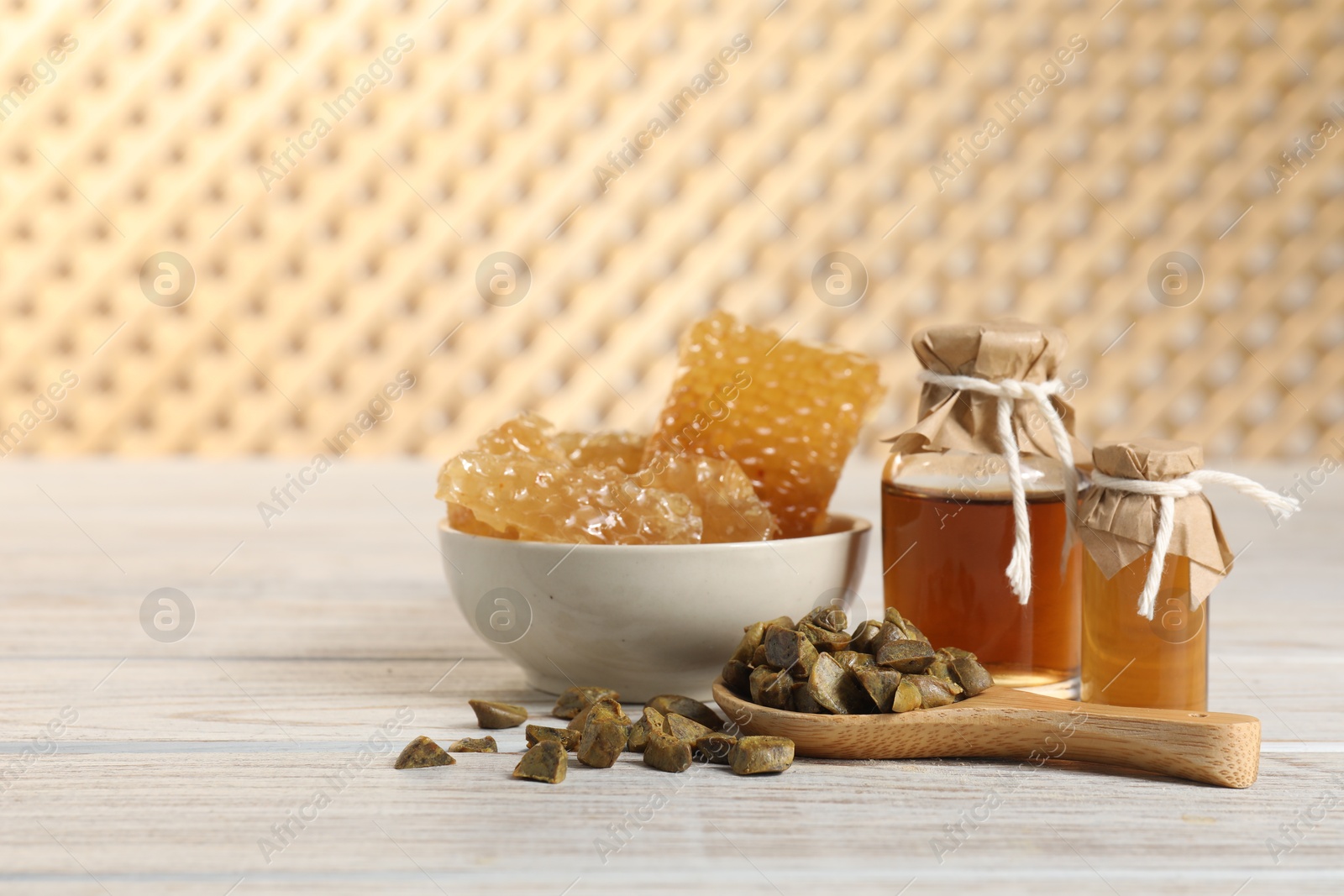 Photo of Natural honey tincture, propolis granules and sweet honeycombs on white wooden table, space for text