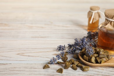 Photo of Natural honey tincture, lavender and propolis granules on white wooden table, closeup. Space for text