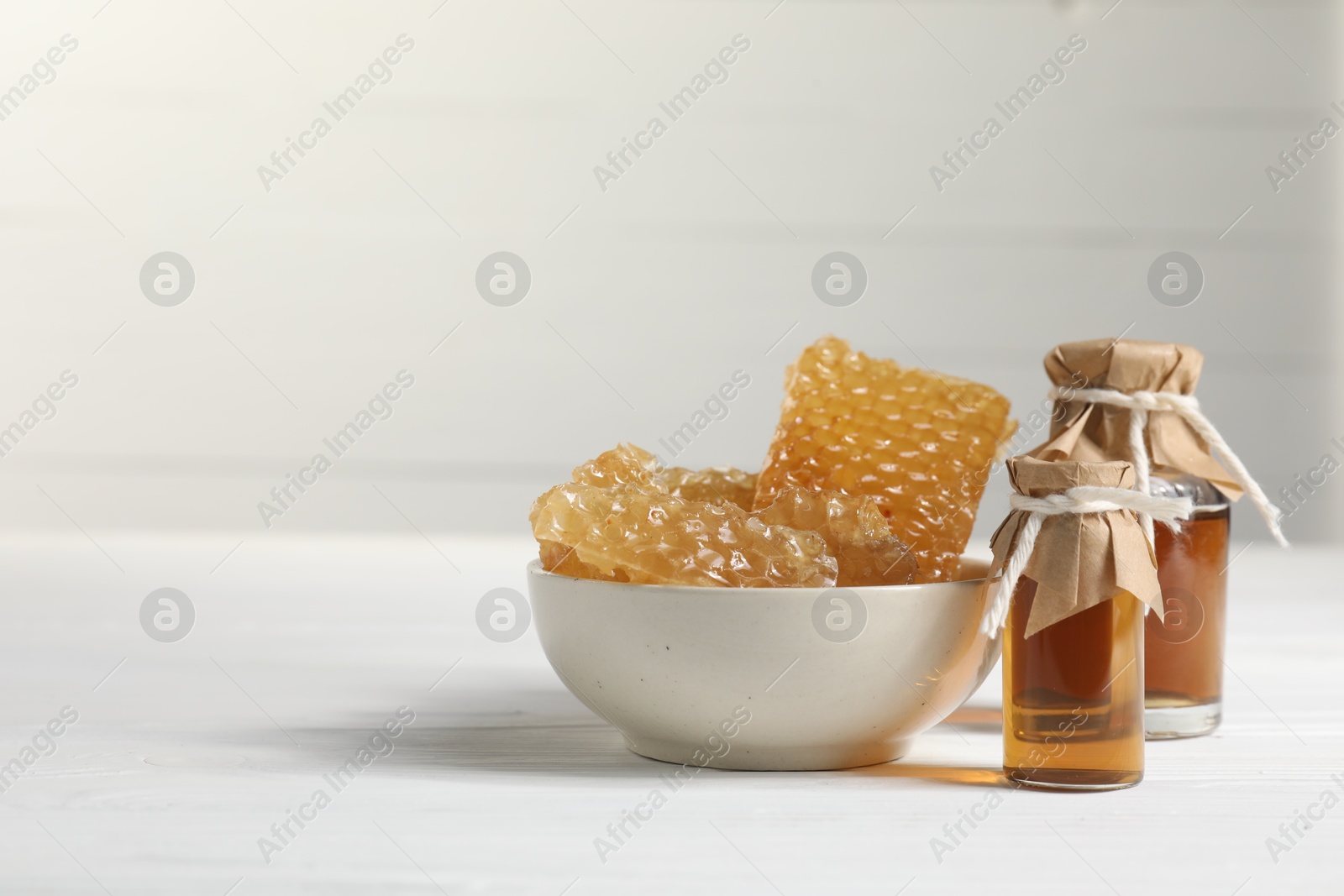 Photo of Natural honey tincture and sweet honeycombs on white wooden table, space for text