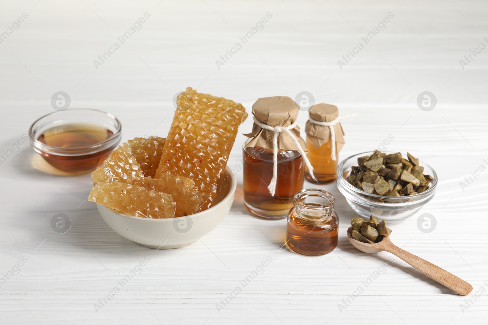 Photo of Natural honey tincture, propolis granules and sweet honeycombs on white wooden table