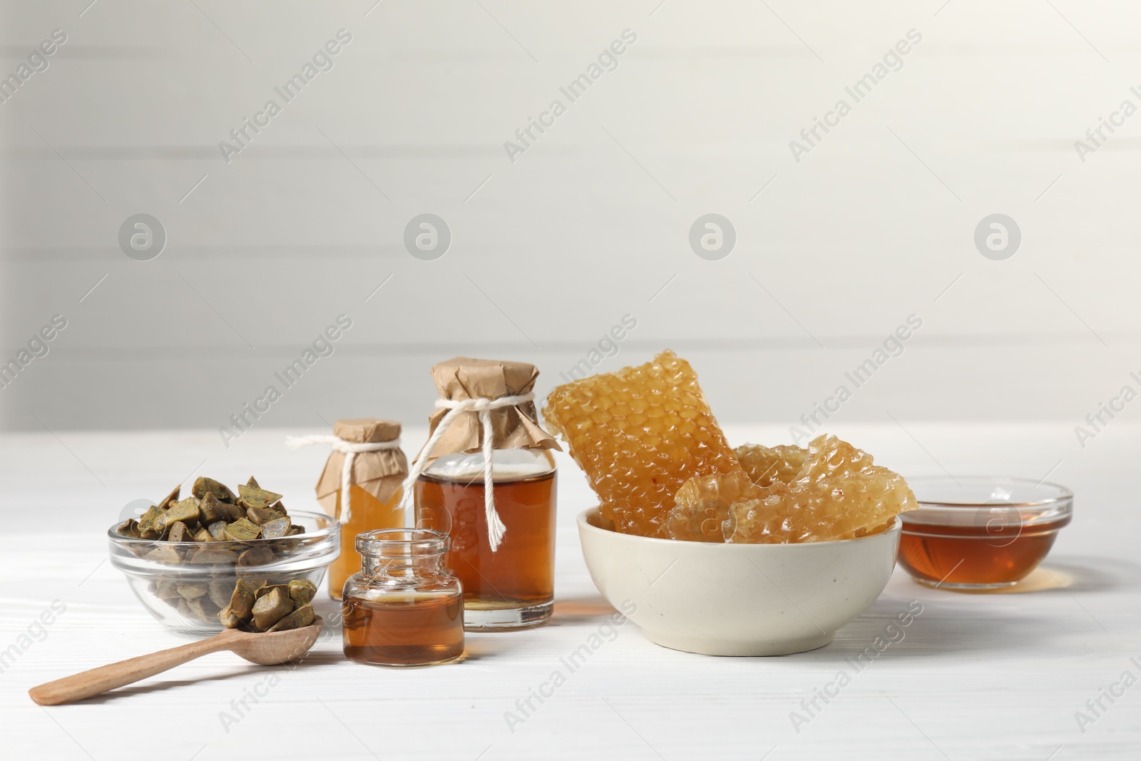 Photo of Natural honey tincture, propolis granules and sweet honeycombs on white wooden table