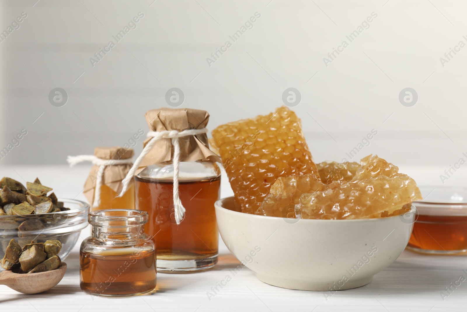 Photo of Natural honey tincture, propolis granules and sweet honeycombs on white wooden table, closeup