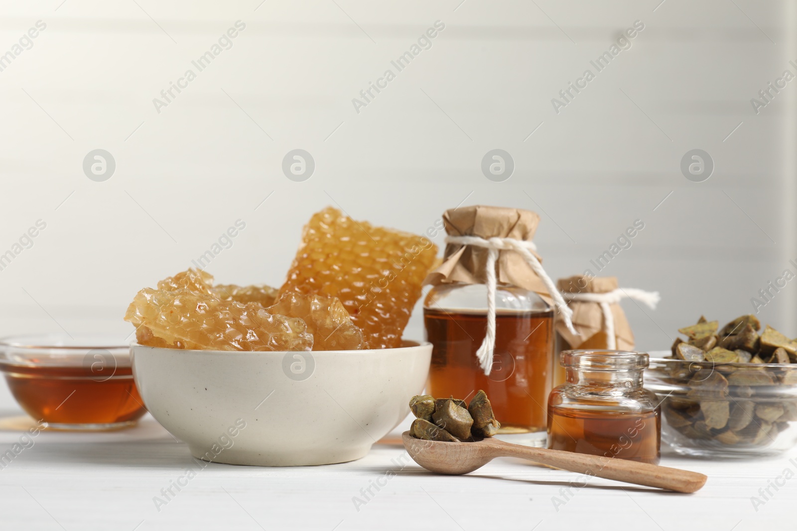 Photo of Natural honey tincture, propolis granules and sweet honeycombs on white wooden table, closeup