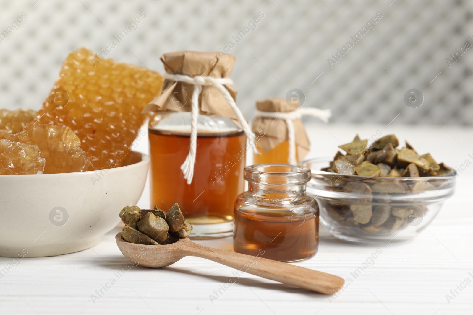 Photo of Natural honey tincture, propolis granules and sweet honeycombs on white wooden table, closeup