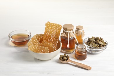 Photo of Natural honey tincture, propolis granules and sweet honeycombs on white wooden table