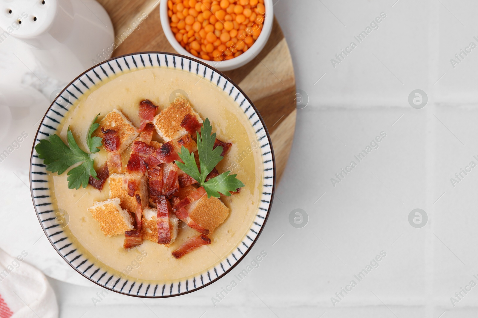 Photo of Delicious lentil soup with bacon and parsley in bowl on white tiled table, flat lay. Space for text