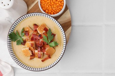 Photo of Delicious lentil soup with bacon and parsley in bowl on white tiled table, flat lay. Space for text