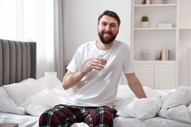 Photo of Happy man with glass of water on bed at morning