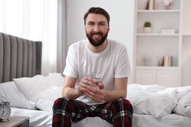 Photo of Happy man with glass of water on bed at morning