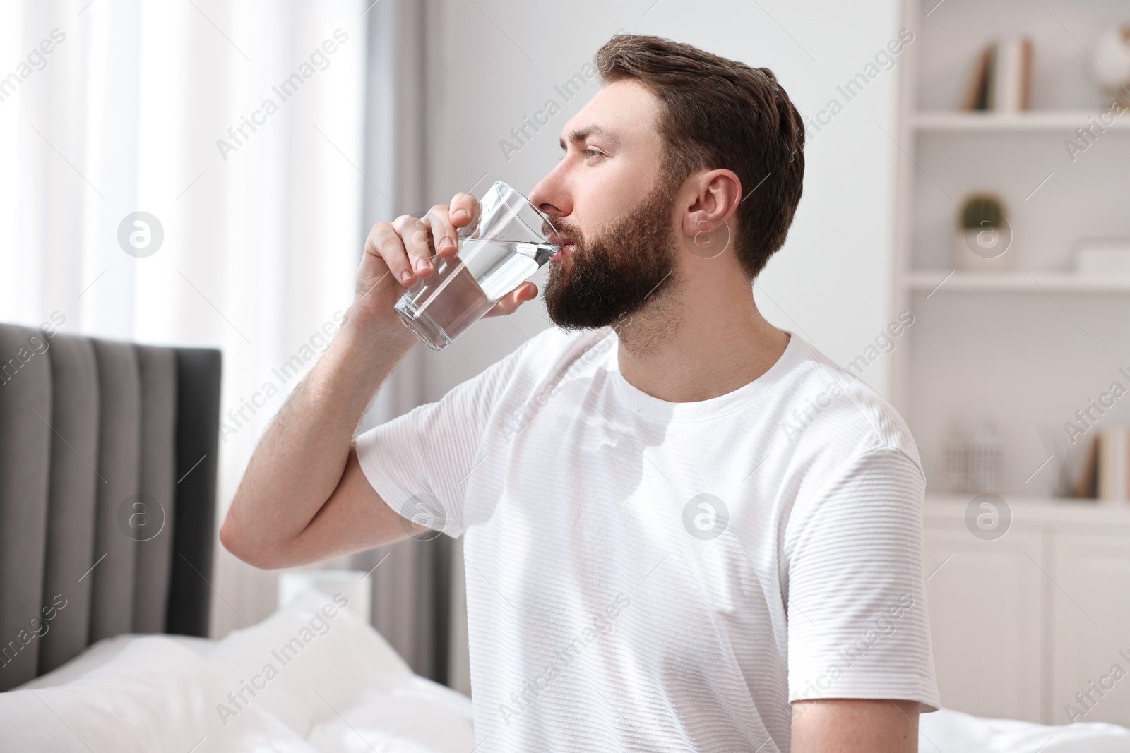 Photo of Happy man with glass of water on bed at morning