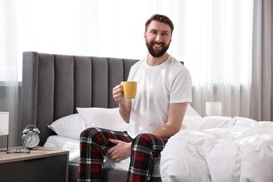 Photo of Happy young man with cup of coffee on bed at morning
