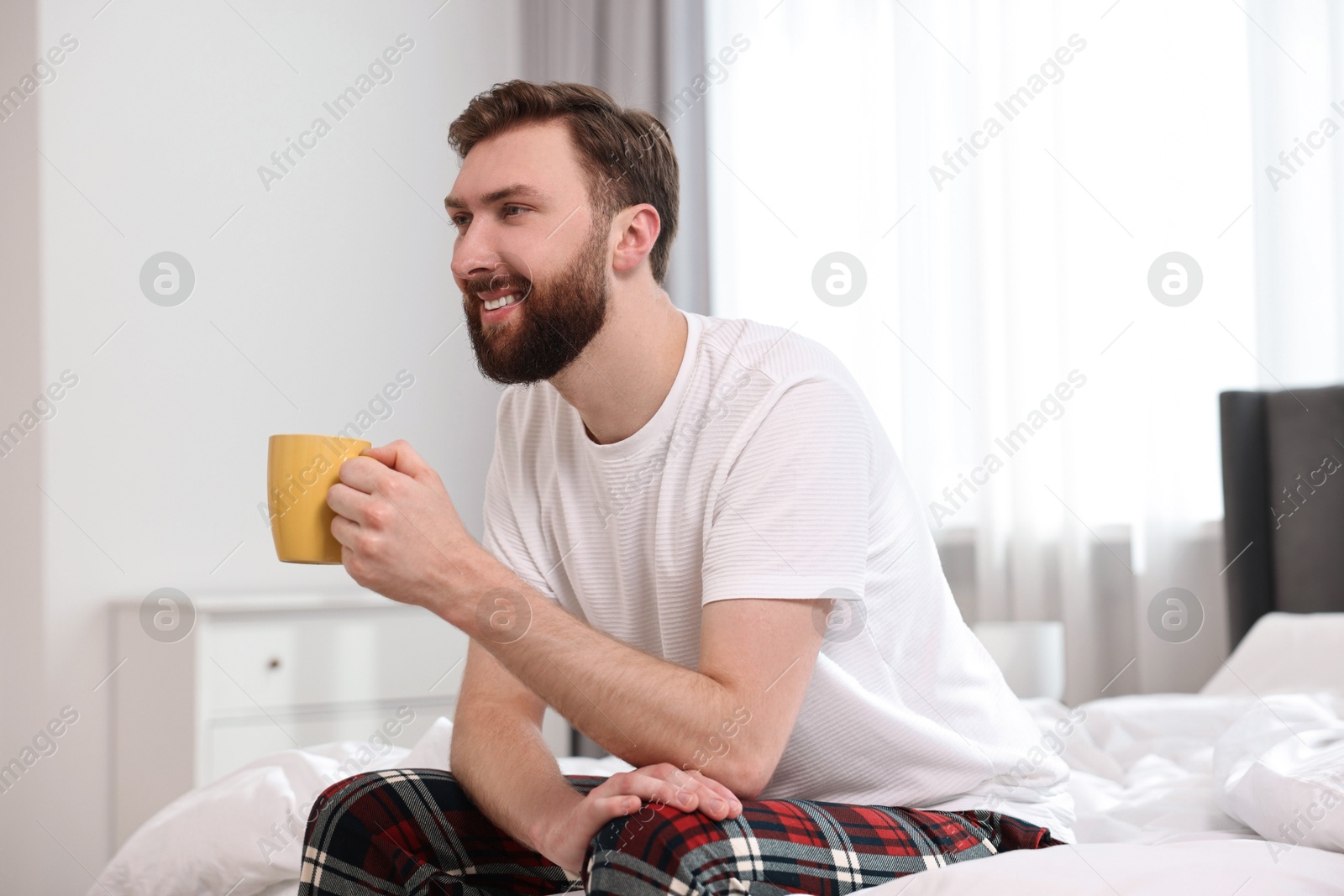 Photo of Happy young man with cup of coffee on bed at morning