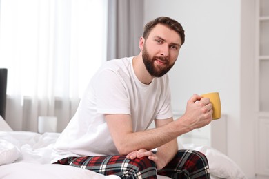 Photo of Happy young man with cup of coffee on bed at morning