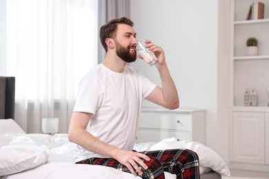Photo of Happy young man with glass of water near on bed at morning