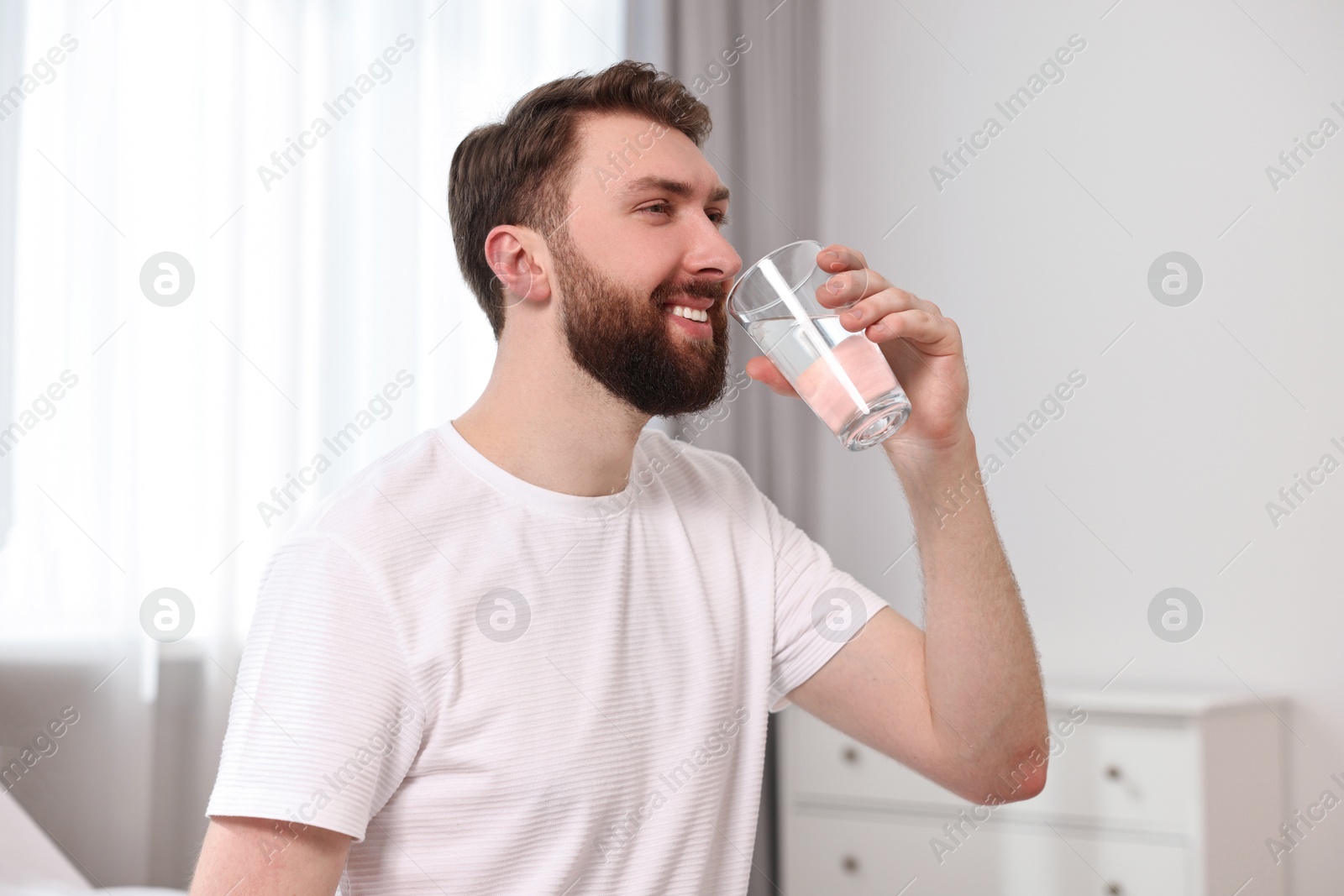 Photo of Happy young man with glass of water near on bed at morning