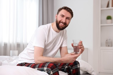 Photo of Happy young man with glass of water near on bed at morning